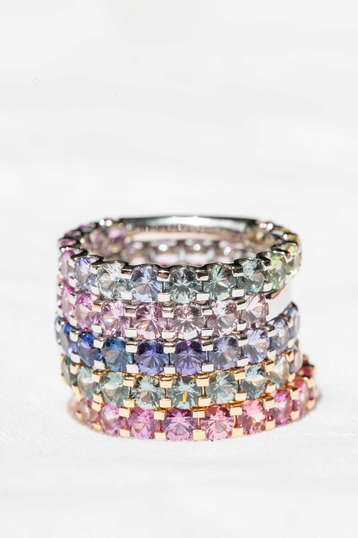 AI ALT: 18ct gold ring with ombre Ceylon sapphires in blue, pink, purple, green, yellow hues; elegant stacked design on white background.